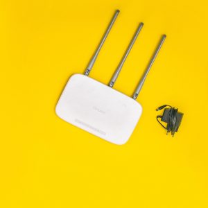 White router with three antennas and cables on bold yellow background, ideal for tech concepts.